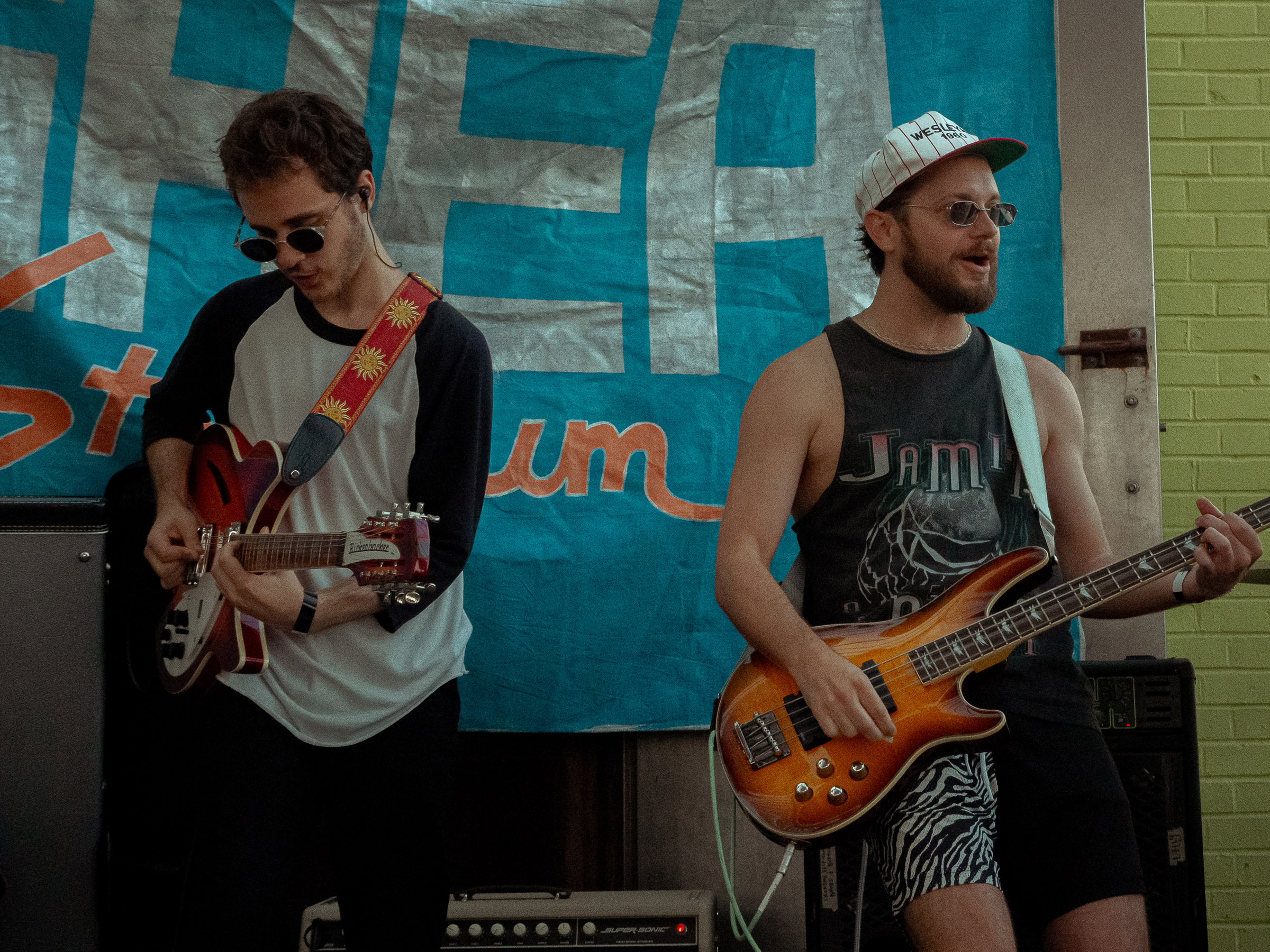 Guitarist, Trevor, and bassist, Ethan, play in front of blue Shea Stadium banner.